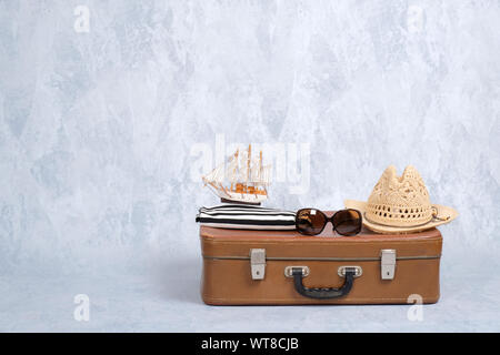 Altmodische leder Reisetasche mit Sommer marine Zubehör: Gläser, Stroh Beach Hut, Spielzeug Segelboot auf grauem Hintergrund. Banner mockup mit Kopie sp Stockfoto