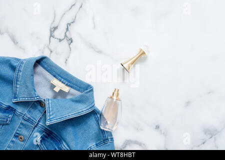 Jeansjacke und Flasche Parfüm auf Marmor Hintergrund. Flach design Zusammensetzung mit weiblicher Kleidung und Accessoires. Schönheit blogger, trendigen Hi Stockfoto