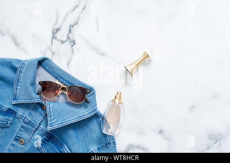 Jeans Jacke, Flasche Parfüm und retro altmodischen Sonnenbrille auf Marmor Hintergrund. Flach design Zusammensetzung mit weiblicher Kleidung und Zubehör Stockfoto