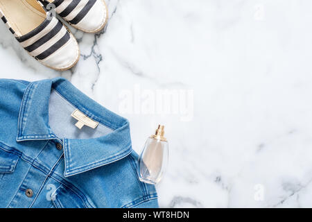 Jeans Jacke, Flasche Parfüm, gestreifte Sommer Sandalen auf Marmor Hintergrund. Flach design Komposition mit Retro altmodische weibliche Kleidung und ein Stockfoto