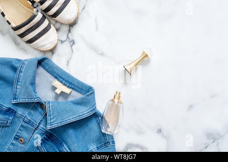 Grenze der Jeans Jacke, Flasche Parfüm, gestreifte Sandalen auf Marmor Hintergrund. Flach design Zusammensetzung mit weiblicher Kleidung und Accessor Stockfoto