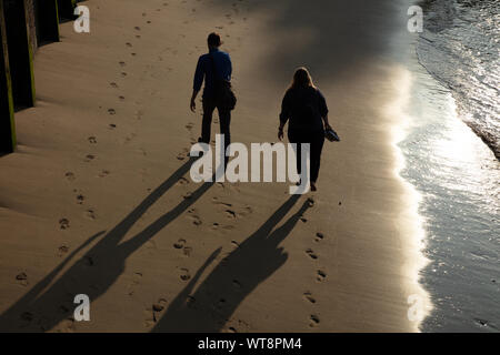 Silhouetten von zwei Menschen zu Fuß am Sandstrand der Themse in London am späten Tag im Sommer. Stockfoto
