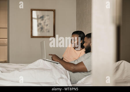 Lächelnden jungen afrikanischen amerikanischen Paar mit einem Laptop im Bett Stockfoto