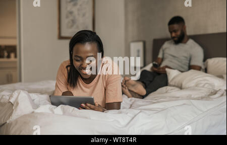Lächelnd afrikanische amerikanische Frau im Bett liegend mit einem Tablet Stockfoto