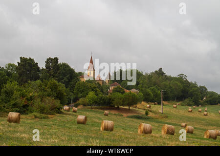 Kreisförmige strawbales auf einem Feld, im Hintergrund die Kirche und mittelalterlichen Torhaus des Dorfes Pouylebon in Südwest Frankreich