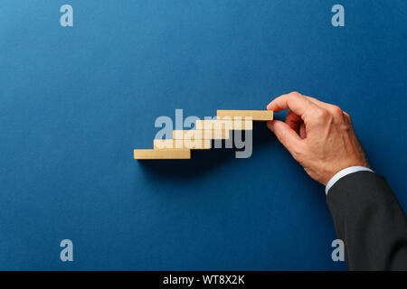 Hand, ein Geschäftsmann, eine Treppe wie Struktur aus Holz in einem konzeptionellen Bild pegs. Über Marine blauen Hintergrund. Stockfoto