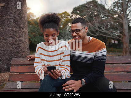 Porträt eines afrikanischen jungen Paar zusammen Standortwahl auf der Bank im Park am Handy suchen Stockfoto