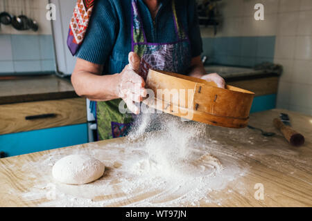 Großmutter kochen, Hand der alten Frau sichten Mehl durch ein Sieb auf den Teig. Stockfoto