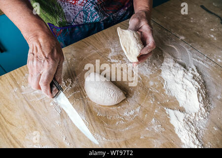 Ältere Frau Bäcker schneiden Teig in Home Küche Stockfoto