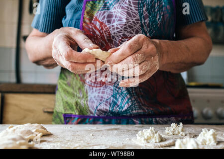 Vorbereitung Teigtaschen mit Quark gefüllt. Ältere weibliche Hände, pierogi oder pyrohy, Wareniki, vareniki. Traditionelle russische Küche, Bäckerei Stockfoto