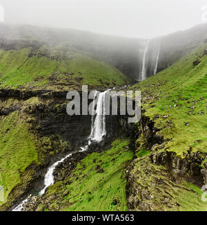 Dicken Nebel schwebende über grüne moosige Böschung und kühlen Wasserfall an trüben Tag auf den Färöer Inseln Stockfoto