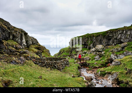 Einsamer Reisender auf Holzbrücke über Mountain Creek fluß an grünen felsige Tal in düsteren Tag Stockfoto