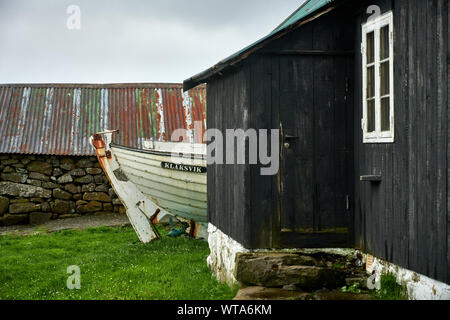 Rustikale Holzhaus mit alten weißen Boot und Stein auf düsteren Tag in der Landschaft der Halle auf den Färöer Inseln Stockfoto