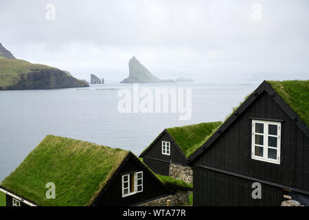 Küstenlandschaft von kleinen Holzhäuser mit Bemoosten grünen Gras auf Dächern gegen misty Felsen im Meer Stockfoto
