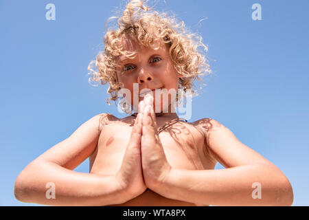 Blonde lockige schwarzhaarige Junge meditiert am Strand Stockfoto