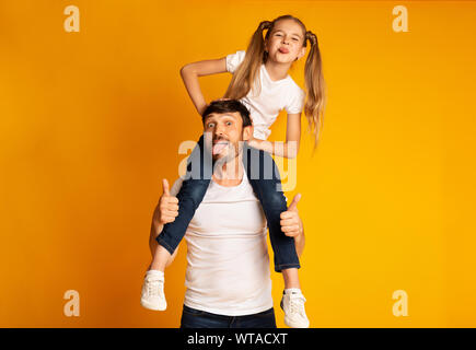 Mann, der Tochter auf die Schulter und Gestikulierte Thumbs-Up Übersicht Zungen, Studio Stockfoto