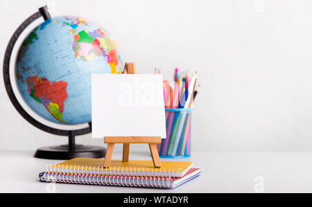 Kleine Staffelei mit klaren Blatt Papier und andere Verbrauchsmaterialien auf Weiß Stockfoto