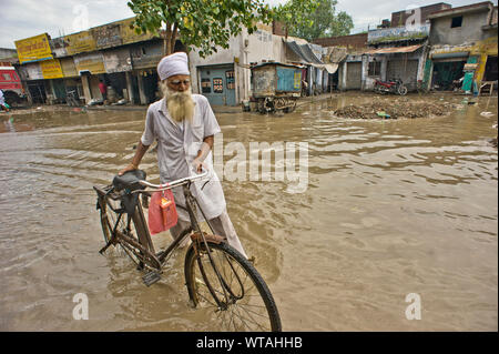 Sikh Mann sein Fahrrad mit auf den Straßen in einer Flut Tag Stockfoto