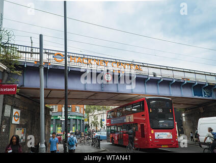 Red London Bus unter einer Eisenbahnbrücke mit signage für Hackney Central S-Bahn Station im Mare St, Hackney, East London, UK Stockfoto