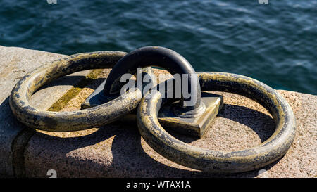 Close-up Low Angle View von zwei rostige verwitterte Liegeplatz Ringe auf Stein Wand neben Wasser Stockfoto