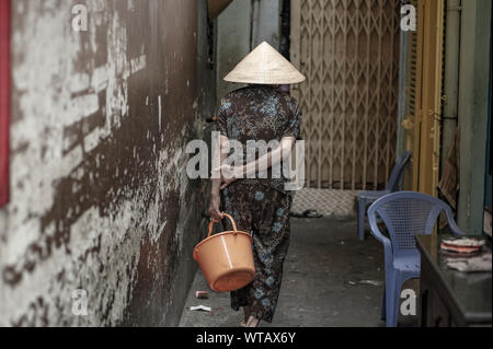 Alte Frau trägt La Nao hat eine Schaufel in Saigon Gassen Stockfoto