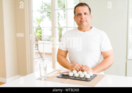 Mittleres Alter mann Essen asiatische Knödel zu Hause mit ernsten Gesichtsausdruck. Einfache und natürliche in die Kamera schaut. Stockfoto