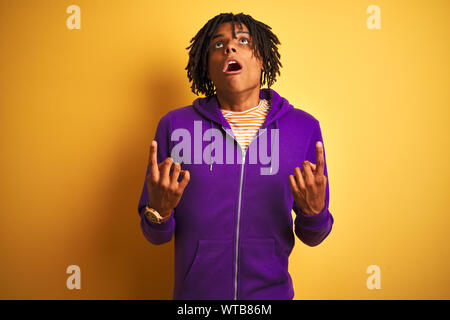 Afro-amerikanische Mann mit Dreadlocks tragen lila Sweatshirt über isolierte lila Hintergrund erstaunt und überrascht mit der Suche und zeigt mit Fingern, Stockfoto