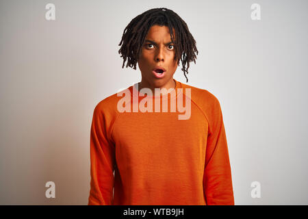 Afro-amerikanische Mann mit Dreadlocks tragen Orange Pullover über isoliert weißer Hintergrund Angst und mit Erstaunen Ausdruck, Angst schockiert und aufgeregt Stockfoto
