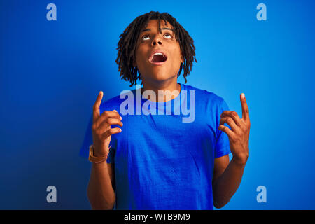Afro-amerikanische Mann mit Dreadlocks tragende t-shirt stehend über isolierte blauen Hintergrund erstaunt und überrascht mit der Suche und zeigt mit Fingern und Stockfoto