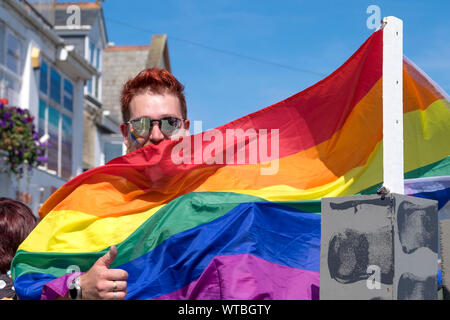 Ein Mann in einer Gay Pride Regenbogen Flagge in der Cornwall Pride Parade Teilnahme an Newquay in Cornwall gewickelt. Stockfoto