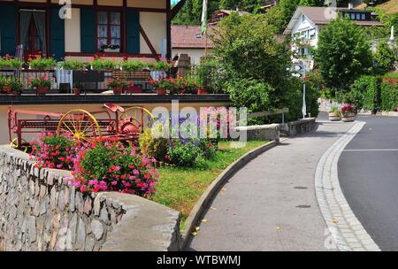Blick auf einen wunderschönen gestalteten kleinen Garten an der Straße, die das Dorf in den Waadtländer Alpen überquert Stockfoto