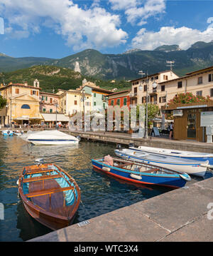 MALCESINE, Italien, 13. Juni 2019: Der kleine Hafen am Ufer des Lago di Garda See mit dem 2000 m hohen Bergen im Hintergrund. Stockfoto