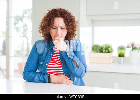 Ältere Frau mittleren Alters mit lockigem Haar zu tragen Jeans Jacke zu Hause Unwohlsein und als Symptom für kalte oder Bronchitis Husten. Healthcare Konzept Stockfoto