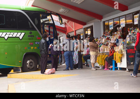 BANOS, Ecuador - 22. FEBRUAR 2014: Nicht identifizierte Personen am Busbahnhof mit dem Bus, der in der Rückseite und Imbissbuden auf der Seite Stockfoto