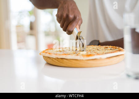 Nahaufnahme der afrikanischen Mann schneidet ein Stück Käse Pizza mit einem Cutter Stockfoto