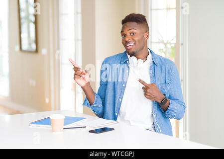 African American student Mann lernen mit Notebooks und das Tragen von Kopfhörern und lächelnd in die Kamera zeigte mit zwei Händen und Fingern zu suchen Stockfoto