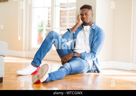 African American man mit Kopfhörern Musik hören auf dem Boden sitzend Denken müde und gelangweilt mit Depressionen Probleme mit gekreuzten Stockfoto