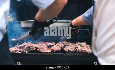 Zwei Köche kochen Fleisch vom Grill, Picknick mit Grillen im Freien. Fleisch gebraten auf Metallgitter. Die person Kochen Fleisch. Kochen Fleisch auf dem gr Stockfoto
