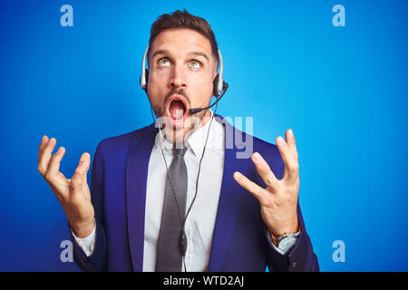 Junge schöne operator Mann mit Call center Headset über Blau isoliert Hintergrund verrückt und wütenden Schreien und Kreischen mit aggressiven Ausdruck ein Stockfoto