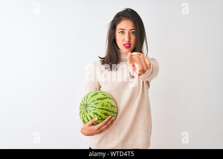 Junge schöne chinesische Frau mit Wassermelone stehend über isoliert weißer Hintergrund zeigt mit dem Finger auf die Kamera und an Sie, Hand, Zeichen, pos Stockfoto
