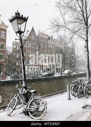 Snowy Fahrräder auf der Brücke im Zentrum der Stadt Amsterdam, Niederlande. Blizzard auf Winter in den Niederlanden. Fahrräder mit Schnee auf einer Brücke abgedeckt. Stockfoto