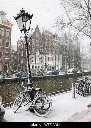 Snowy Fahrräder auf der Brücke im Zentrum der Stadt Amsterdam, Niederlande. Blizzard auf Winter in den Niederlanden. Fahrräder mit Schnee auf einer Brücke abgedeckt. Stockfoto