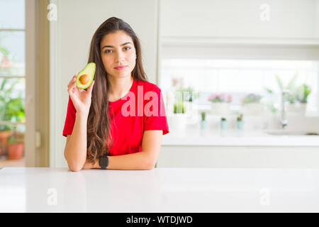 Junge Frau gesund essen Avocado mit einem selbstbewussten Ausdruck auf Smart Face denken Ernst Stockfoto