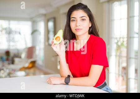 Junge Frau gesund essen Avocado mit einem selbstbewussten Ausdruck auf Smart Face denken Ernst Stockfoto