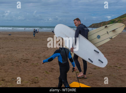 Vater und Sohn tragen Taucheranzüge, die auf dem Saunton Sands, North Devon, England, Großbritannien surfen Stockfoto