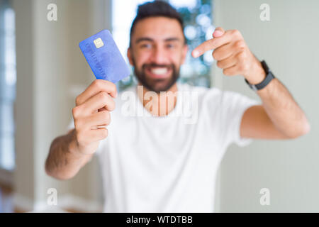 Stattliche Hispanic Mann mit Kreditkarte sehr glücklich zeigte mit Hand und Finger Stockfoto