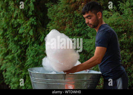 Junger Mann herstellen und verkaufen von Zuckerwatte auf eine Gasse im Park auf einem Festival in Bukarest, Rumänien, 2019 Stockfoto