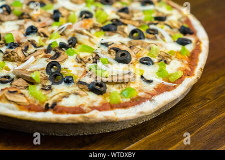 Nahaufnahme der hausgemachten leckeren Pizza mit Pilzen Oliven Zwiebel, Paprika und Käse Pizza auf ein Brett auf einem alten rustikalen Küche aus Holz Tische serviert. Stockfoto