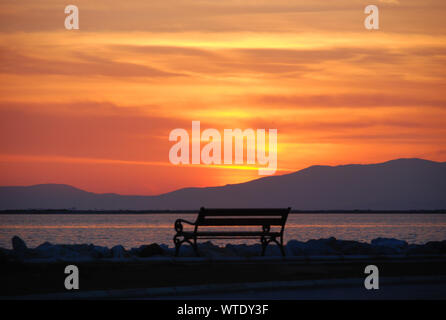 Leeren Bank mit Blick auf das bunte Licht des Sonnenuntergangs über dem Horizont auf das Ägäische Meer an der Küste von Izmir, Türkei Stockfoto