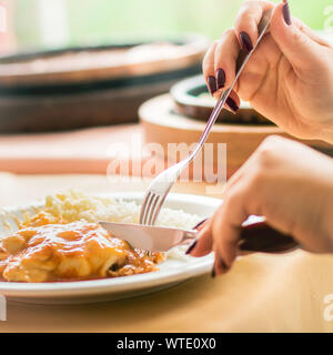 Foto einer Frau schneiden ein Stück Hühnchen Parmigiana in einem Restaurant. Stockfoto